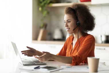 Telekonferans. Mutfakta dizüstü bilgisayarla video görüşmesi yapan siyah kadın kameraya gülümseyen ve hareket eden Afro-Amerikan kadın çevrimiçi iletişimin tadını çıkaran,