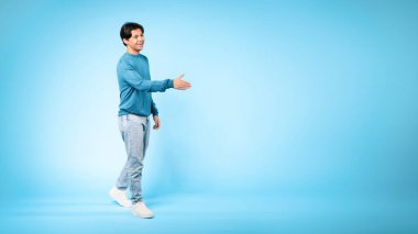 Hoş geldiniz. Arkadaş canlısı Asyalı genç adamın el sıkışmak için elini uzatması ve Blue Studio 'nun arka planında boş alanın yanında durması. Tanıştığımıza memnun oldum, Reklam Sancağı.