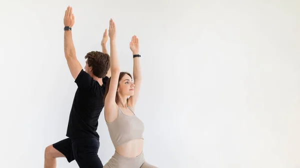 积极镇定的年轻的欧洲女士和穿着运动服的家伙练习瑜伽 在灰色背景下与跟踪器一起做呼吸练习 运动和健身 一起锻炼 — 图库照片