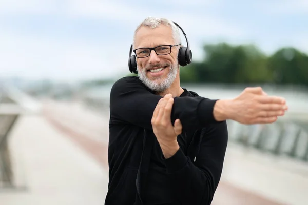 Happy elderly man stretching arms and smiling in park with music. Senior sportsman, outdoor runner and motivation for fitness, energy and healthy exercise training with headhones, copy space