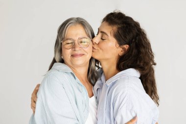 Neşeli olgun bir kadın yaşlı bir bayanın yanağından sarılıp öpüyor, anne kızının ziyaretinden zevk alıyor, beyaz stüdyo arka planında soyutlanıyor. Aile sevgisi, kadın nesli, ilişki ve yaşam tarzı