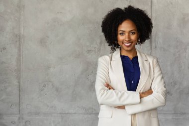 Kurumsal iş kadını neşeli çekici bin yıllık Afro-Amerikan kadın gür saçlı, resmi takım elbiseli, kolları göğsünde gri mermer duvarın üzerinde duruyor ofis binasında, uzay fotokopisini çekiyor.