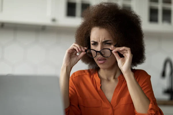 Black freelancer woman with bad eyesight taking off glasses while using laptop at home, young african american female looking at computer screen and squinting, having vision troubles, closeup