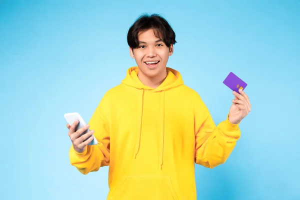 オンラインショッピングアプリ 携帯電話やクレジットカードを使って若い日本人の10代の若者を笑顔 青のスタジオの背景にWebストアで購入 リモートバンキングとインターネット販売のコンセプト — ストック写真