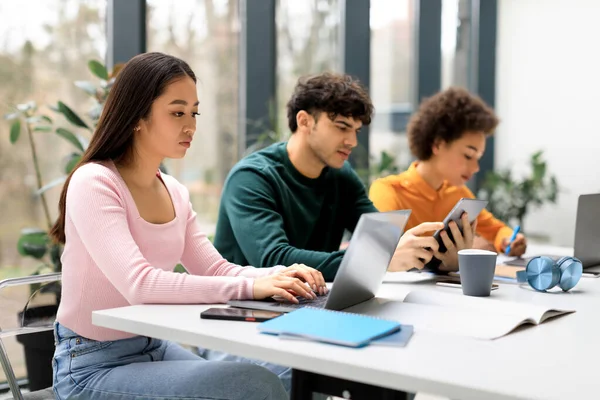 一组不同的学生一起学习考试 一起做项目或一起做作业 用笔记本电脑把注意力集中在一位亚裔女士身上 坐在一起工作的桌旁 — 图库照片