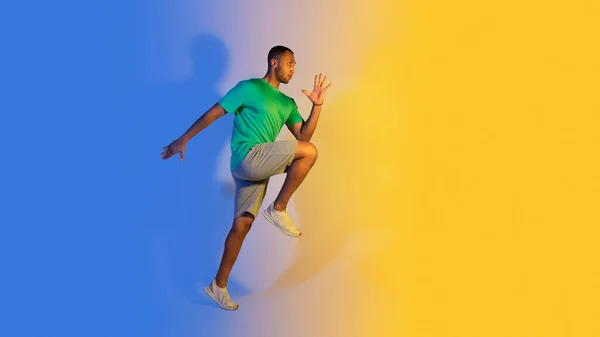 青と黄色の背景 サイドビュー上の空中で実行されているスポーティアフリカ系アメリカ人の若い選手の男性 フィットネスワークアウト中にフィットネスウェアを着たランナー男 フリースペースのパノラマ — ストック写真