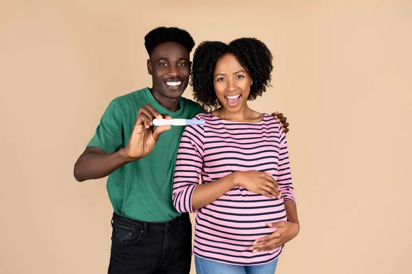 Uśmiechnięta Afrykańska Para Tysiąclecia Pokazująca Test Ciążowy Wyizolowana Beżowym Tle — Zdjęcie stockowe