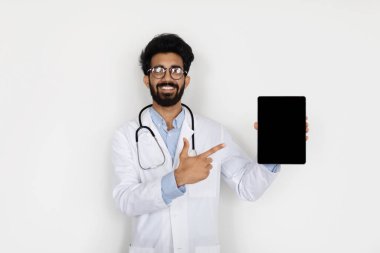 Uzaktan sağlık hizmeti, teletıp, online yardım konsepti. Tıp alanında çalışan yakışıklı genç Arap doktor dijital tableti siyah boş ekran, maket, kopyalama alanı ile gösteriyor.