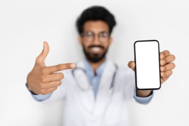 Doktorun elinde beyaz boş ekran maketi olan akıllı telefon. Neşeli Orta Doğulu genç doktor uzak sağlık hizmetleri için en yeni mobil uygulamayı öneriyor, doktor konseptiyle online randevu