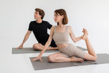 Spor giyimli sakin Avrupalı bir çift bacak egzersizi yapıyor, gri arka planda yoga yapıyor. Kilo kaybı, egzersiz, sağlık ve spor yaşam tarzı
