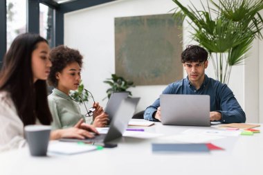 İş şirketi. Modern ofis içinde birlikte çalışan çok kültürlü bir ekip dizüstü bilgisayarların başında oturmuş büyük bir masada oturuyorlar. Şirket İşbirliği ve Takım Çalışması