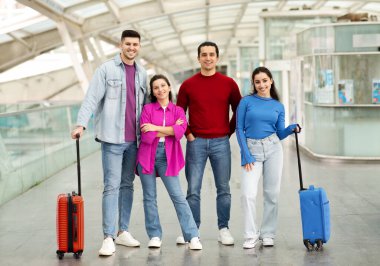 Çanta Ekibi. İki mutlu çift, bavulları ile kucaklaşarak modern havalimanında kameraya bakarak tatil için poz veriyorlar. Seyahat teklifi reklamı. Tam Uzunluk Çekimi