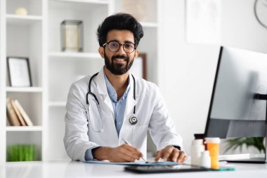 Dost canlısı gülümseyen, tıbbi ceket giyen, gözlüklü, ensesinde steteskop olan yakışıklı genç adam. Modern klinikteki ofisinde çalışan aile doktoru, reçete yazan, fotokopi çeken.