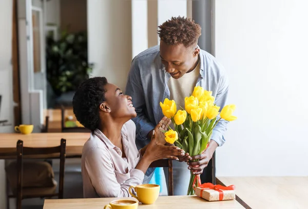 美丽快乐的年轻黑人夫妇在餐馆里有浪漫的约会 可爱的非洲裔美国人 带着鲜花和礼品盒来到他兴奋的女友的咖啡馆 — 图库照片