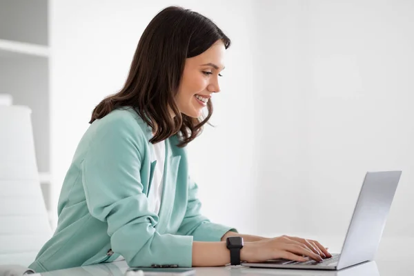 笑着穿西服的年轻欧裔女士在笔记本电脑上打字 与现代办公室内部的客户聊天 女商人和女商人 有设备的职业 生活方式 — 图库照片