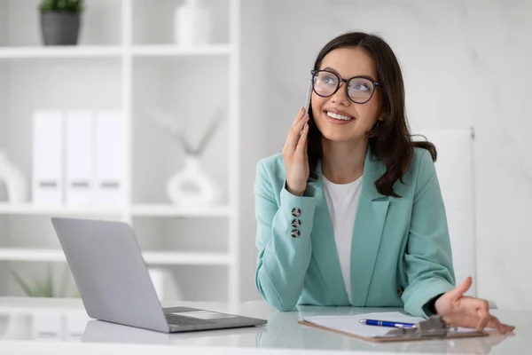 身穿眼镜和西服 头戴手提电脑的快乐的年轻欧裔女性 在现代办公室里打电话 女商人与成功的商业 客户沟通 工作和生活方式 — 图库照片