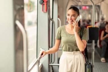 Modern tramvayın içinde cep telefonuyla konuşan mutlu yolcu bayan, uzaklara bakıyor. Genç bir kadın toplu taşımacılıktan zevk alıyor işe gidip gelirken iletişim kuruyor. Boşluğu Kopyala