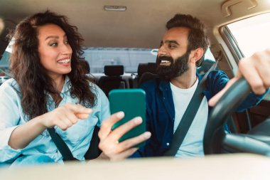 Yaz tatili. Gülümseyen Arap çift lüks arabanın içinde oturuyor, akıllı telefon tutan neşeli adam ve dijital harita uygulaması kullanarak ekranı işaret eden kadın.