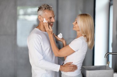 Mutlu ve olgun bir çift birlikte banyoda vakit geçiriyorlar kocalarının yüzüne köpük banyosu yaptırıp gülüyorlar evde güzellik rutini yapan romantik yaşlı eşler ve bedava uzay programları yapıyorlar.