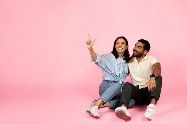 色鮮やかなピンクのスタジオの背景に隔離された広告やテキストのためのコピースペースを指して 床に座って受け入れ若いヒスパニック系のカップルを愛する幸せ 二人分の旅行契約 — ストック写真