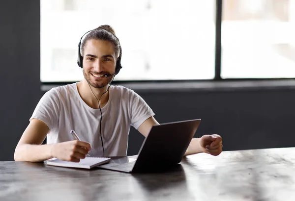 Sonriente Joven Hispano Sentado Computadora Portátil Usando Auriculares Mientras Trabaja —  Fotos de Stock