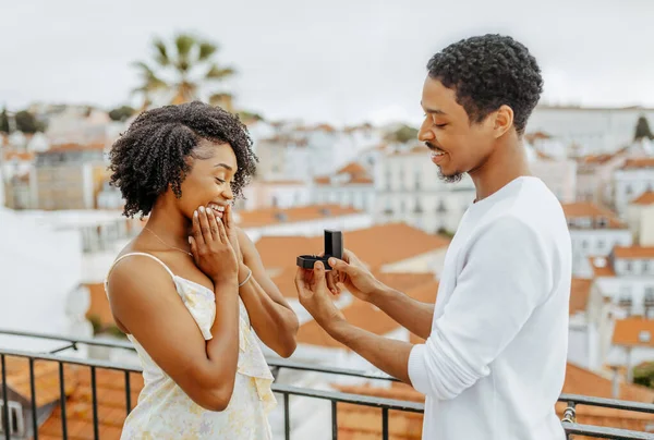 Cheerful young african american man open box with ring, proposes to surprised lady in city, enjoy date and travel, outdoor. Engagement, love, relationships, vacations and romance