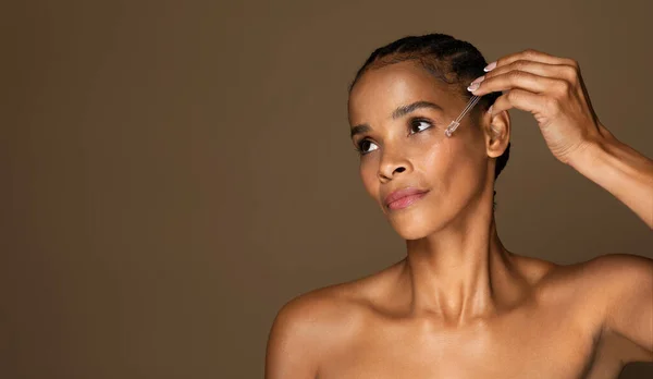 迷人的非洲中年女性 皮肤完美 面部涂有血清 背景呈褐色 复制空间 美容护理 化妆品和温泉抗衰老治疗 — 图库照片