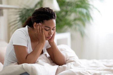 Depresyondaki genç üzgün zenci kadın portresi evde yatağında oturuyor, yorgun Afrikalı Amerikalı kadın baş ağrısı, stres ve uykusuzluk çekiyor, üzgün kadın hissizleşiyor, boşluğu taklit ediyor.