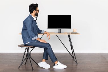 Mutlu gülümseyen genç bir Arap 'ın bilgisayar başında boş siyah ekranlı bir makete bakışıyla. Ev ofisinin masasında oturan Doğulu adam, boş yer. İnsanlar, teknoloji, uzaktan çalışma konsepti