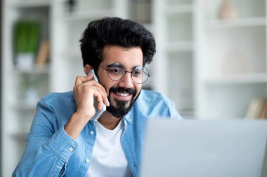 Cep telefonuyla konuşan ve İçişleri Bakanlığı 'nda dizüstü bilgisayar kullanan gülümseyen Hintli adamın yakın plan portresi, doğulu serbest çalışan yakışıklı adam bilgisayar ve ücretsiz uzay üzerinde çalışırken telefon konuşmasının keyfini çıkarıyor.