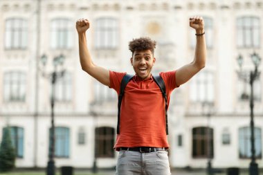 Neşeli Afrikalı Amerikalı öğrenci sınavı geçti, dışarıda üniversite binasının yanında dururken el kol hareketi yaptı, mutlu çömez yumrukları salladı ve 