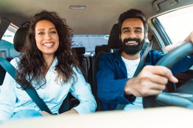 Mutlu araba sahipleri Orta Doğulu karı koca hafta sonu birlikte otomobil yolculuğunun keyfini çıkarıyorlar, emniyet kemerleriyle ön yolcu koltuklarında oturuyorlar, kameraya gülümsüyorlar.