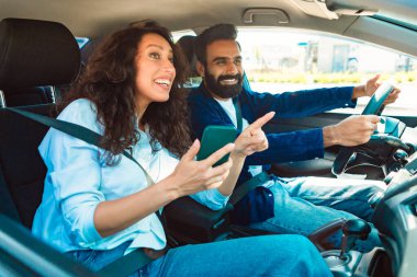Cep telefonu GPS uygulaması kullanarak araba kullanan mutlu bir orta doğulu çift, yeni bir arabada oturuyor ve kadın yolcu sürücünün otomobil sürüşünü gösteriyor.