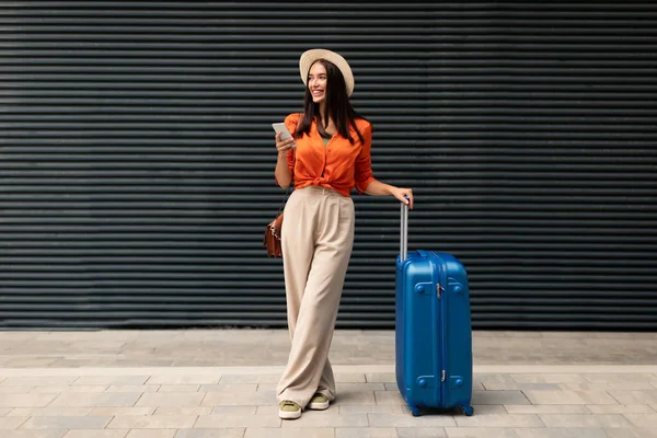 Χαρούμενη Γυναίκα Επιβατών Ταξιδιωτική Βαλίτσα Χρησιμοποιώντας Smartphone Γραπτών Μηνυμάτων Ενώ — Φωτογραφία Αρχείου