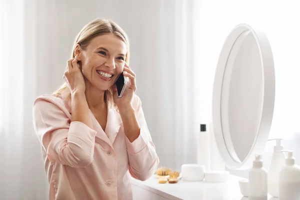 快乐成熟的女性在手机上聊天 坐在家里梳妆台旁 微笑着穿着丝质睡衣的中年妇女享受着愉快的手机交谈 复制空间 — 图库照片