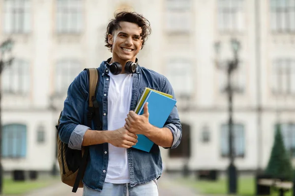 大学の奨学金 バックパックやワークブックを持つ陽気な男性学生の屋外の肖像画 大学の建物の近くに外に立ってハンサムな若い男 コピースペースを見て笑顔 — ストック写真