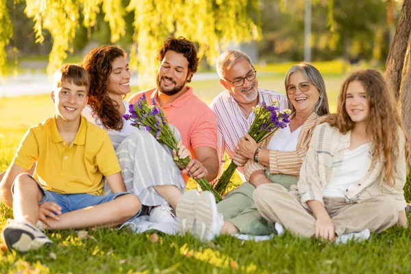快乐的高加索多代人休息 男人送花给女人 享受公园野餐 庆祝节日 在户外聚会 家庭关系 — 图库照片