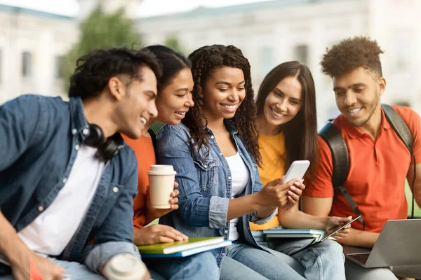 キャンパスレジャー 教室の後は おしゃべりをしたり笑ったりしながら 屋外で一緒にリラックスした学生の多民族グループ 一緒にスマートフォンを使用して幸せな若い多文化の男性と女性 — ストック写真