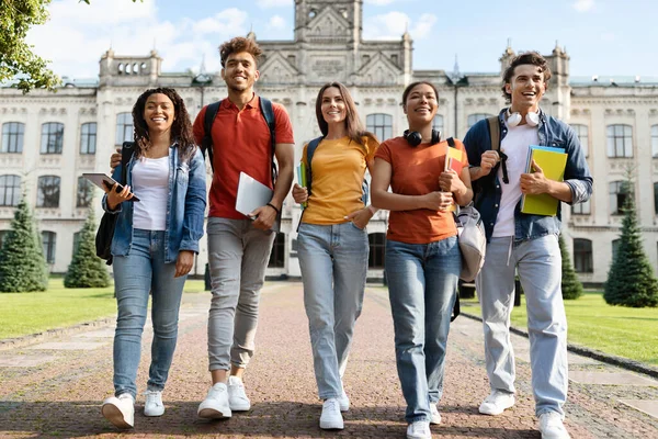University Students Life. Group Of Multiethnic Young People Walking Together Outdoors, Happy Multicultural Friends With Backpacks And Workbooks Going To Campus After Classes, Full Length Shot