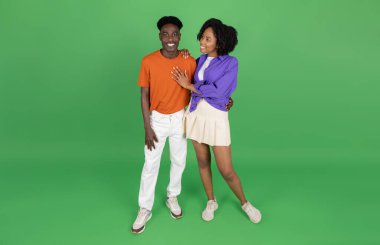 Neşeli genç Afro-Amerikan erkek ve bayan kucaklaşması, buluşmanın keyfini çıkarın, yeşil stüdyo arka planında izole edilmiş, tam boy, panorama. Yaşam tarzı, romantik ilişkiler, birlikte hafta sonu, reklam ve teklif