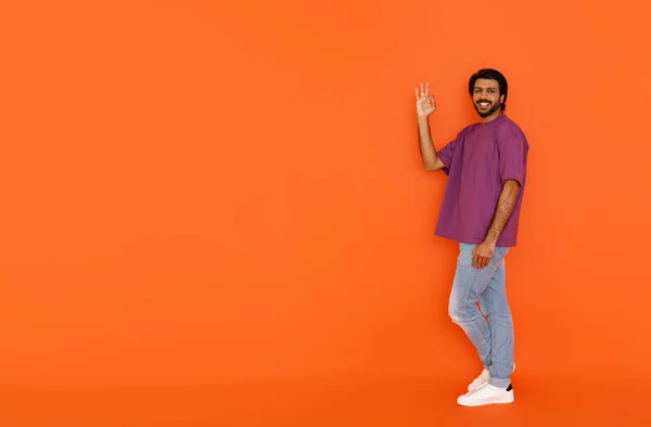 広告や笑顔のためのコピースペースへの正しいジェスチャーを示すカジュアルな幸せなハンサムな若いインド人男性 オレンジのスタジオの背景に隔離されました 素晴らしいオファー 偉大な契約の概念 — ストック写真