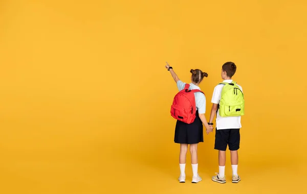 十几岁的欧洲男孩和女孩与背包手拉手 手指在巨大的智能手机与空白的空间 孤立在黄色工作室背景 学校教育 — 图库照片