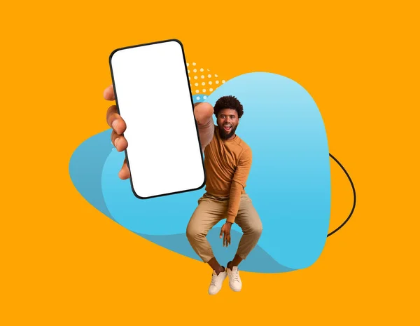 モバイル広告 カラフルな抽象的な背景を飛び越えながら 陽気な黒人男性は 空白の画面で大きなスマートフォンを実証し 幸せな若いアフリカ系アメリカ人の男は空の携帯電話を表示します モックアップ — ストック写真