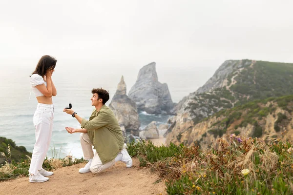 爱在海滨 男人站在他的膝盖上 向在海边岩石悬崖上的女朋友求婚 那是一个令人叹为观止的海岸线 自由自在的空间 — 图库照片