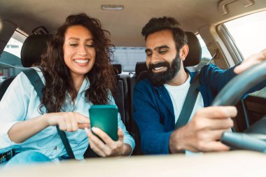 Navigasyon konsepti. Mutlu Arap eşler akıllı telefon kullanarak araba sürüyorlar ve GPS 'i açık bırakıyorlar. Kocasına bir şey gösteren gülümseyen bir kadın.