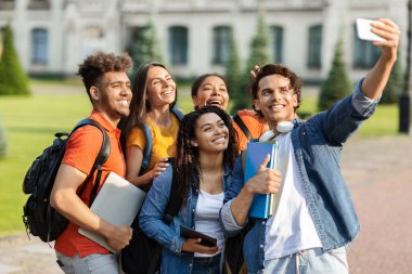 Açık havada akıllı telefondan selfie çeken mutlu çoklu etnik öğrencilerin portresi, cep telefonu kamerasında birlikte poz veren ve dersten sonra dinlenen bir grup neşeli genç üniversite arkadaşı.