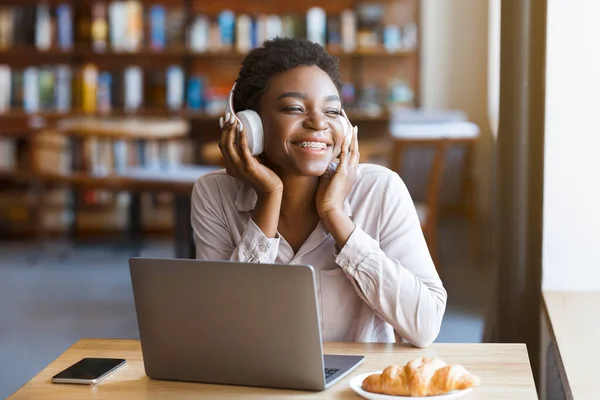 ストレス軽減レジャーコンセプト 美しいアフリカ系アメリカ人の若い女性は 現代のカフェでヘッドセットとコンピュータのラップトップで音楽を聞いて 窓や笑顔 空のスペースを見て — ストック写真