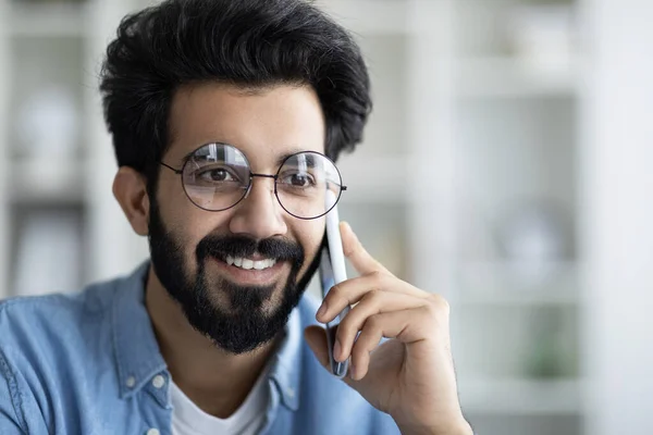 面带微笑的印度小伙子戴着眼镜在讲手机 英俊的千禧年东方人有愉快的交谈和享受移动通信 闭门造车 复制空间 — 图库照片