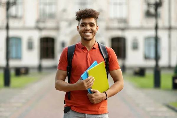陽気な黒の学生の男は バックパックの近くの大学の建物の屋外でポーズワークブックを保持 カメラに微笑む 現代の教育 授業料と助成金 留学と留学の概念 — ストック写真