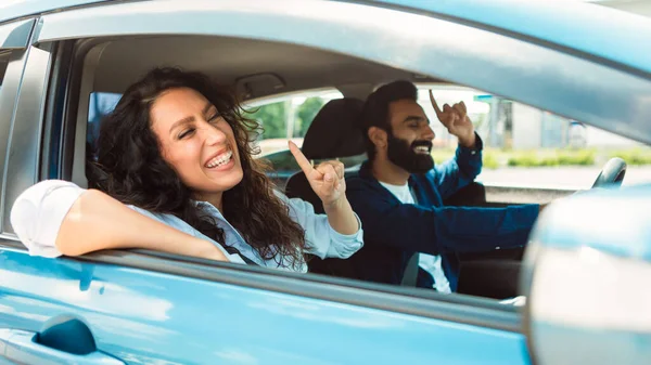 Excited young middle eastern couple enjoying car ride together, arab spouses listening music and dancing in their new auto, celebrating buying modern vehicle